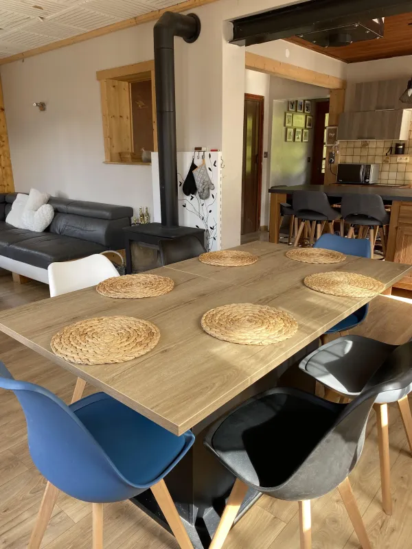 Salle à manger avec salon à côté, poêle à bois, cuisine en arrière plan