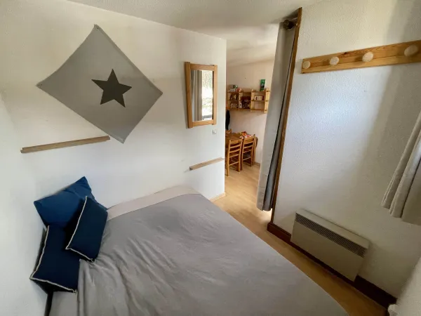 Coin nuit avec lit double, miroir, radiateur et patère, fermeture de la pièce par un rideau