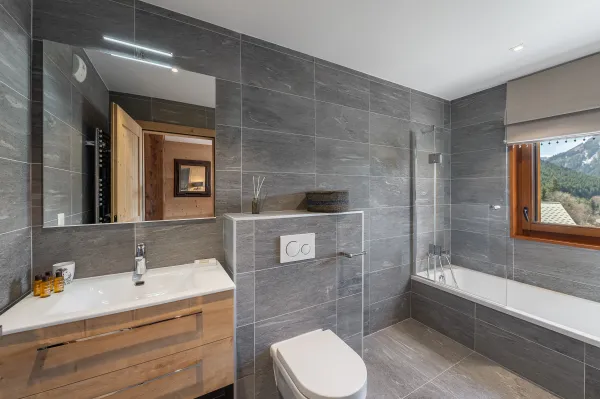 Salle de bains avec baignoire, toilettes, vasque et son meuble, grand miroir, fenêtre